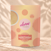 Eleven TLC Ginger Turmeric 500g yellow and peach pouch standing on a travertine ledge against warm plaster, with a contact shadow beneath the base and a soft shadow to the right.