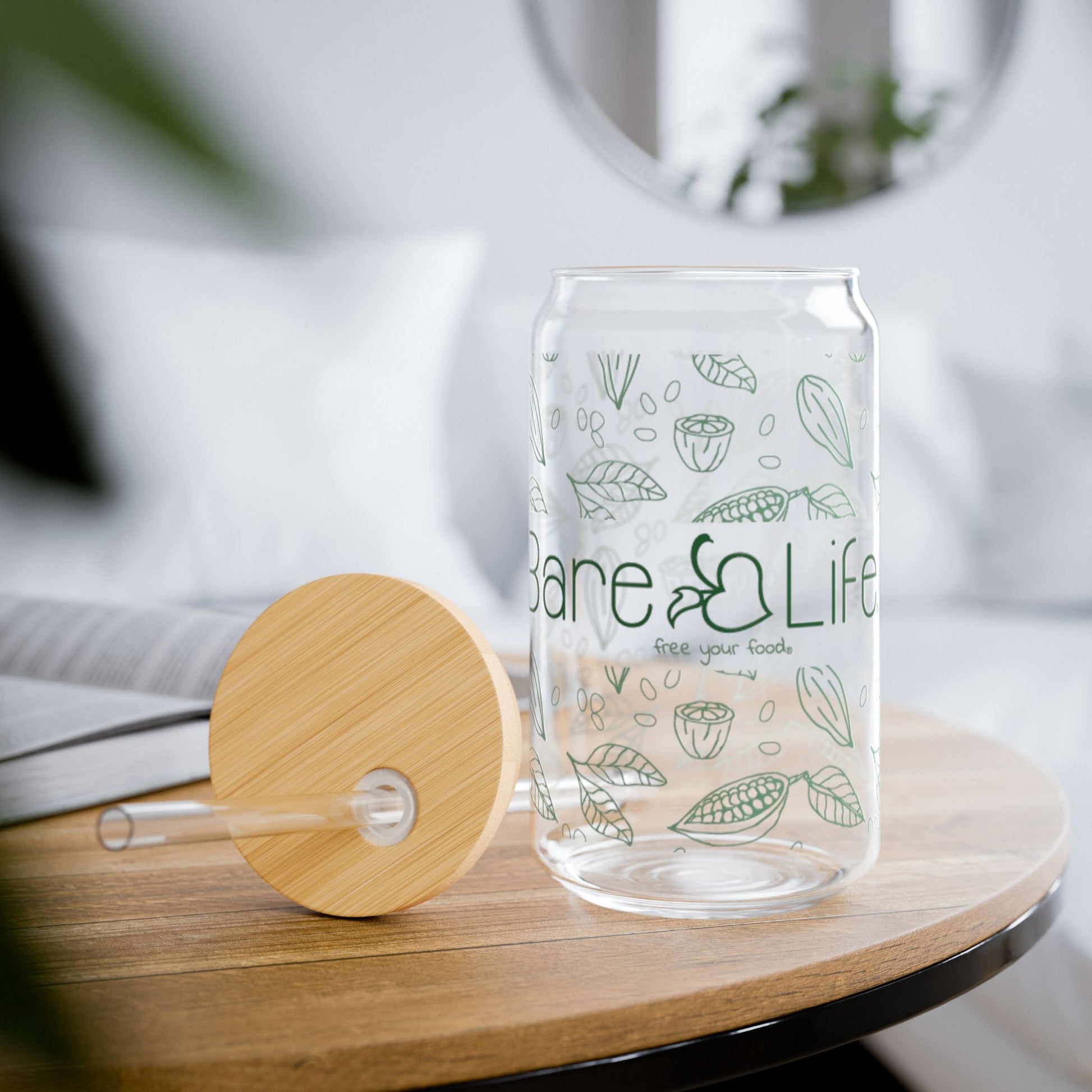 Clear glass tumbler with green leaf patterns and 'Bare Life' branding on a wooden table.