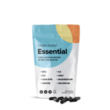 A white, colorful resealable pouch labeled Complement® Essential (Plant Based) multivitamin from Complement stands upright with several black omega-3 capsules scattered in front on a white background.