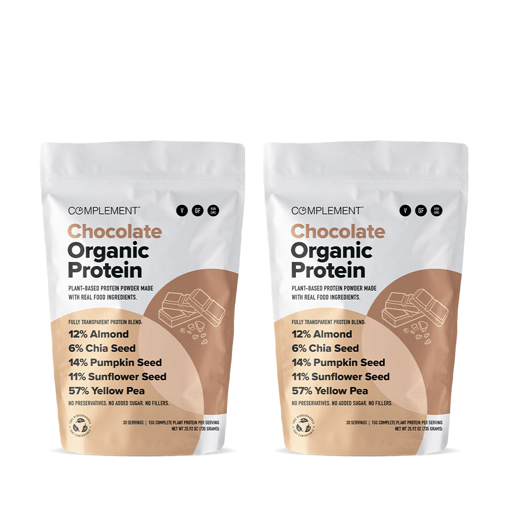 Two bags of Complement brand Chocolate Organic Protein powder are displayed. Each bag highlights ingredients like almond, chia seed, pumpkin seed, sunflower seed, and yellow pea. The bags are white with brown accents and a small chocolate icon.