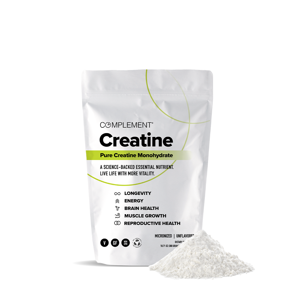A white pouch labeled COMPLEMENT® Creatine from Complement stands upright, with a small mound of white powder in front. The packaging highlights energy, muscle growth, and brain health benefits from premium plant-based creatine.