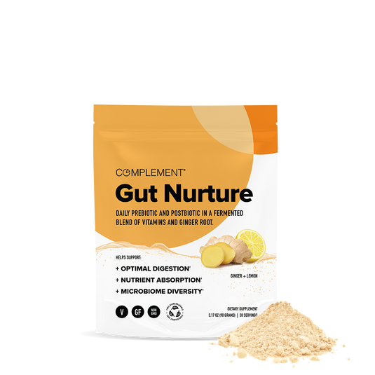 A pouch labeled COMPLEMENT® Gut Nurture by Complement features ginger root and powder images. The packaging highlights digestion support, nutrient absorption, and gut microbiome health. Some prebiotic and postbiotic powder is spilled in front.