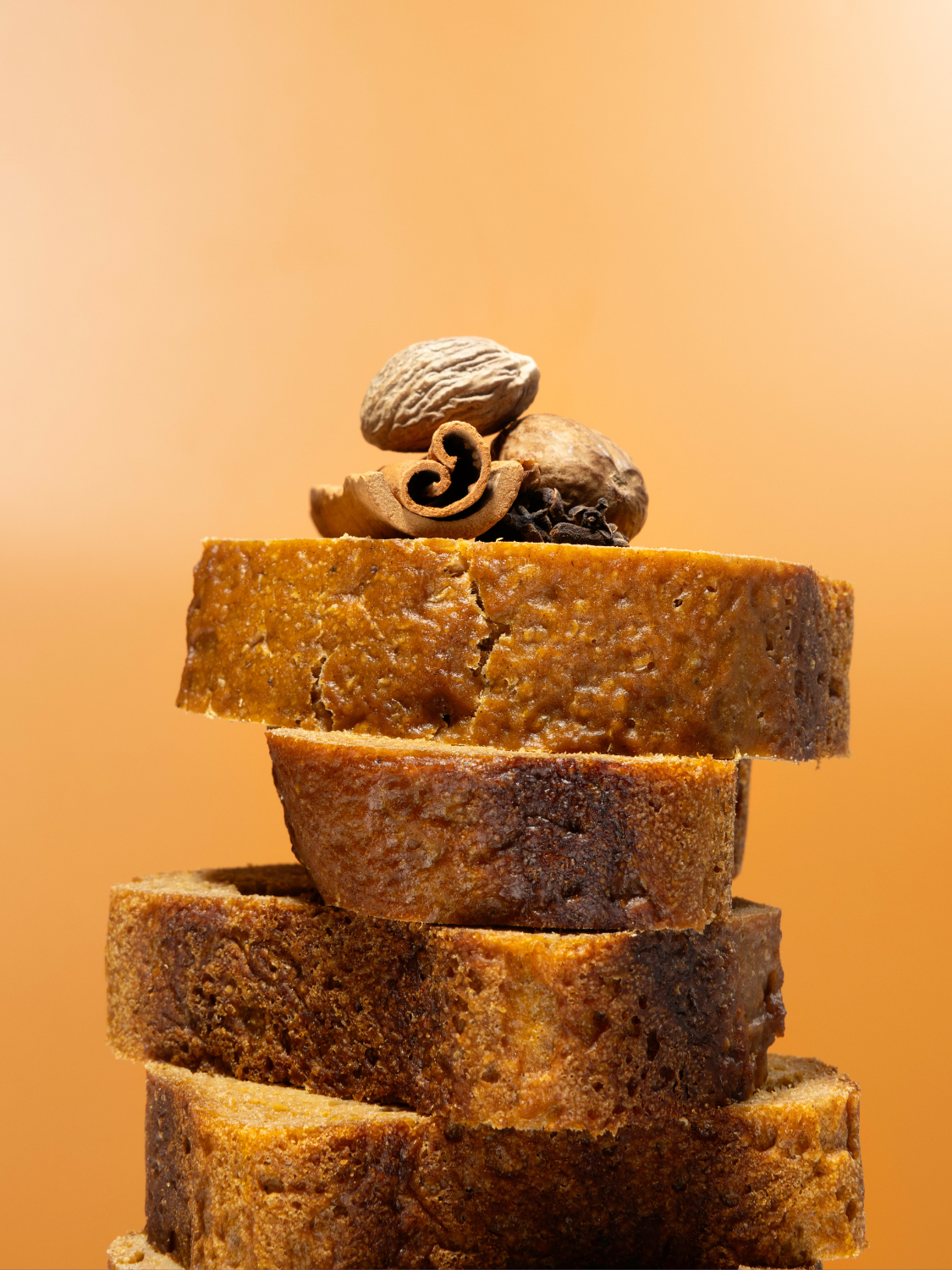 Stack of sliced pumpkin spice bread with spices on top with an orange background