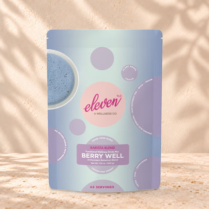 Eleven TLC Berry Well Superfood Latte Mix 500g stand-up pouch on travertine stone against a warm cream plaster wall, lit from the left with a soft shadow to the right.