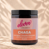 Eleven TLC Organic Chaga Mushroom Powder 82g amber glass jar with a black lid on travertine stone against a warm cream plaster wall, with a soft shadow to the right.
