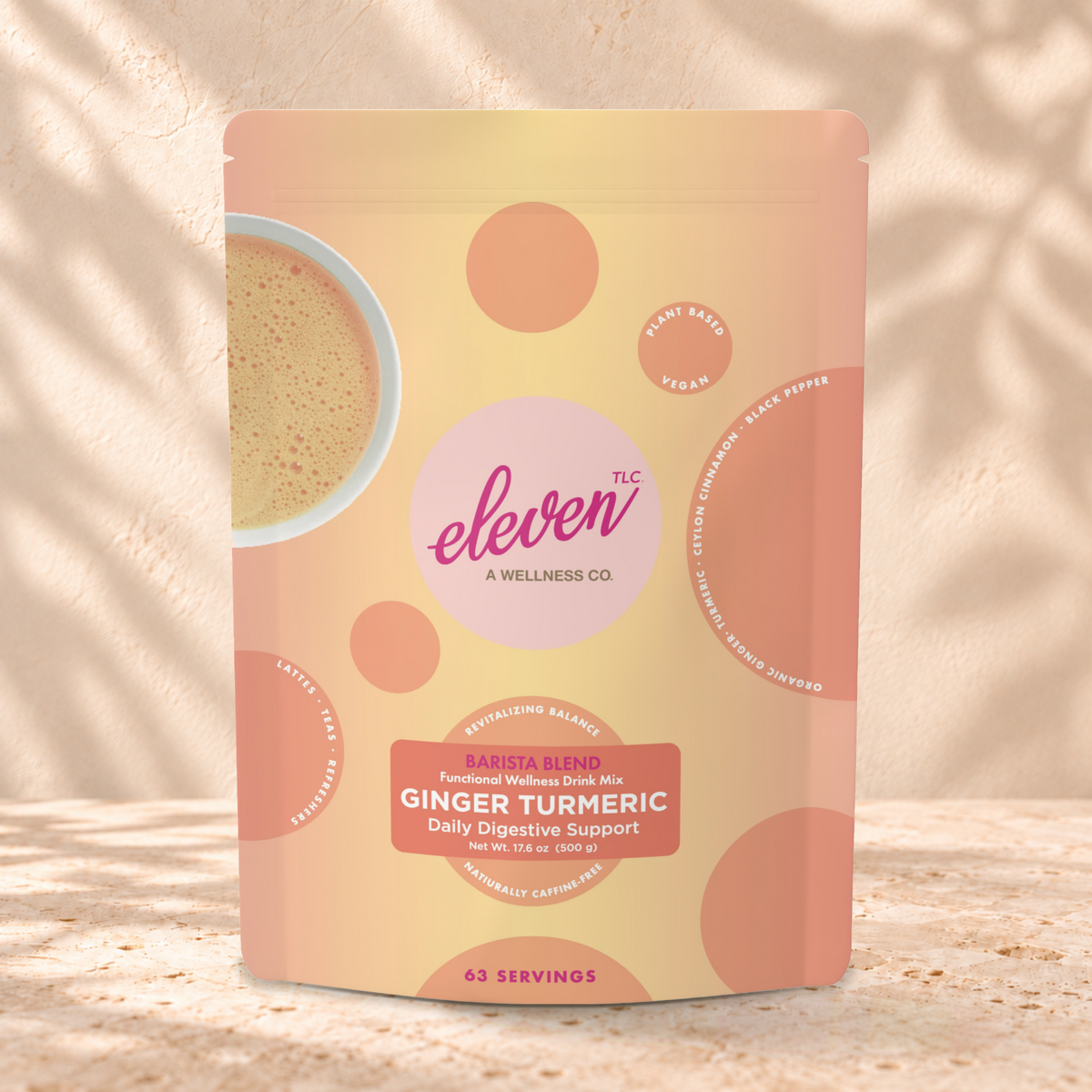 Eleven TLC Ginger Turmeric 500g yellow and peach pouch standing on a travertine ledge against warm plaster, with a contact shadow beneath the base and a soft shadow to the right.