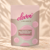 Eleven TLC Maca Root Powder 500g taupe and pink pouch standing on a travertine ledge against warm plaster, with a contact shadow beneath the base and a soft shadow to the right.