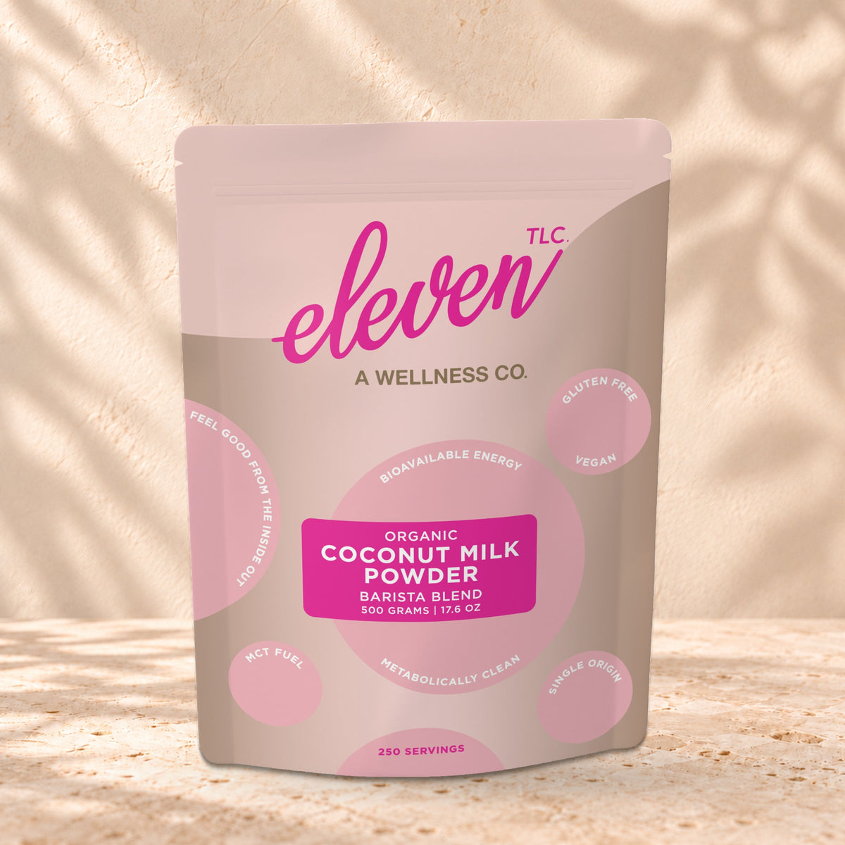 Eleven TLC Coconut Milk Powder 500g stand-up pouch on travertine stone against a warm cream plaster wall, lit from the left with a soft shadow to the right.