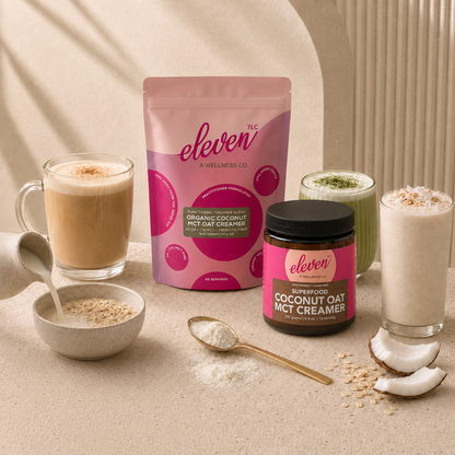 Lifestyle staging on a neutral stone table, featuring the Eleven TLC 500g organic coconut oat mct creamer stand-up pouch and an amber glass jar as the central focal points. The scene includes three glass beverages—a frothy matcha latte, a smooth coffee, and a creamy smoothie—alongside a bowl of oatmeal topped with fresh berries, coconut flakes, and raw oats, illustrating the product's role in a complete nutritional daily signal workflow.