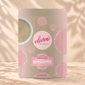 Eleven TLC Shroomie 500g taupe and pink pouch standing on a travertine ledge against warm plaster, with a contact shadow beneath the base and a soft shadow to the right.