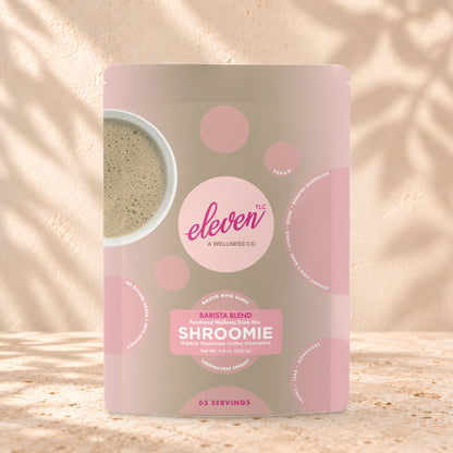 Eleven TLC Shroomie 8-Adaptogen Blend 500g stand-up pouch on travertine stone against a warm cream plaster wall, lit from the left with a soft shadow to the right.