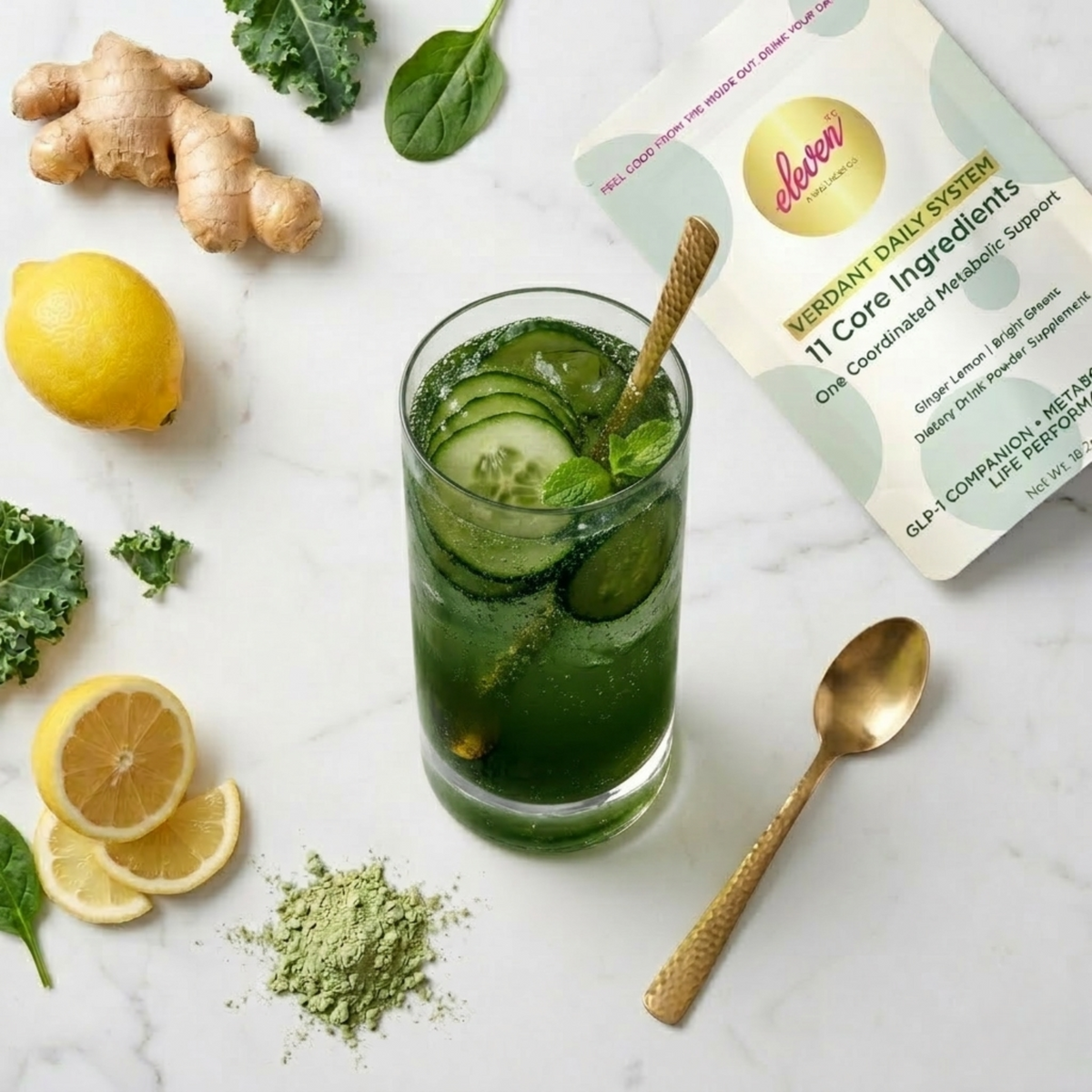 Eleven TLC Verdant Daily System pouch and prepared beverage with fresh ginger, spinach, and lemon on a white marble surface.