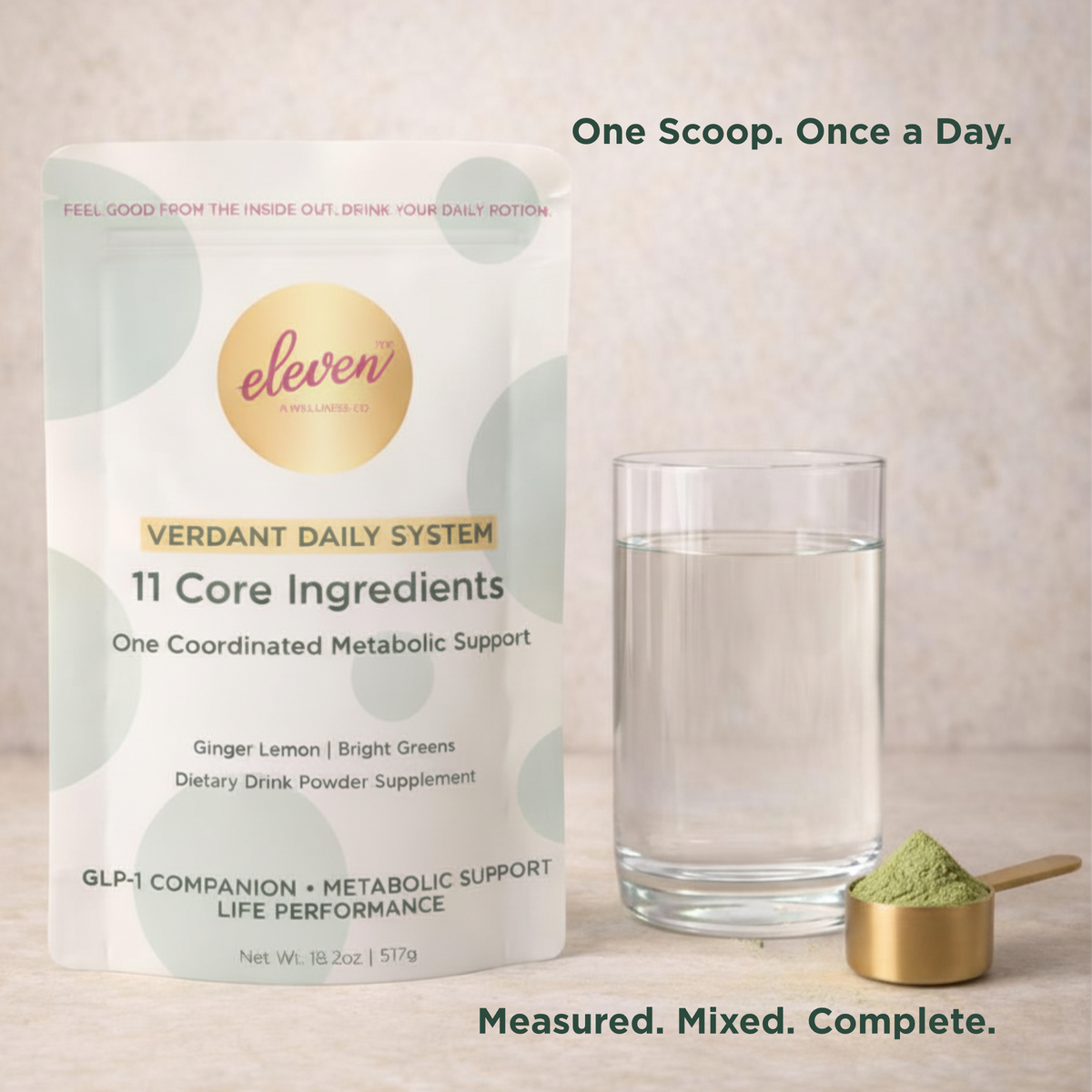 Eleven TLC Verdant Daily System pouch and metallic scoop with powder next to a glass of water on a minimalist stone surface.