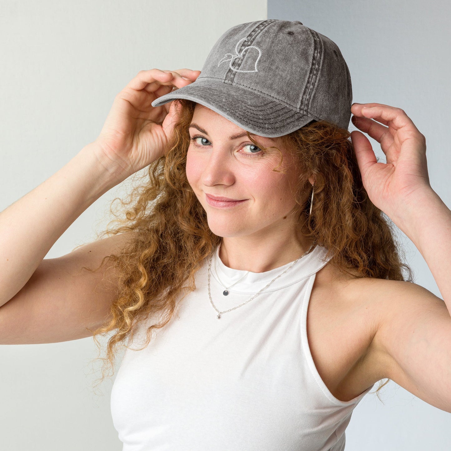 Model adjusting Bare Life’s charcoal gray Cocoa-Chic Cap, smiling and wearing a white tank top.