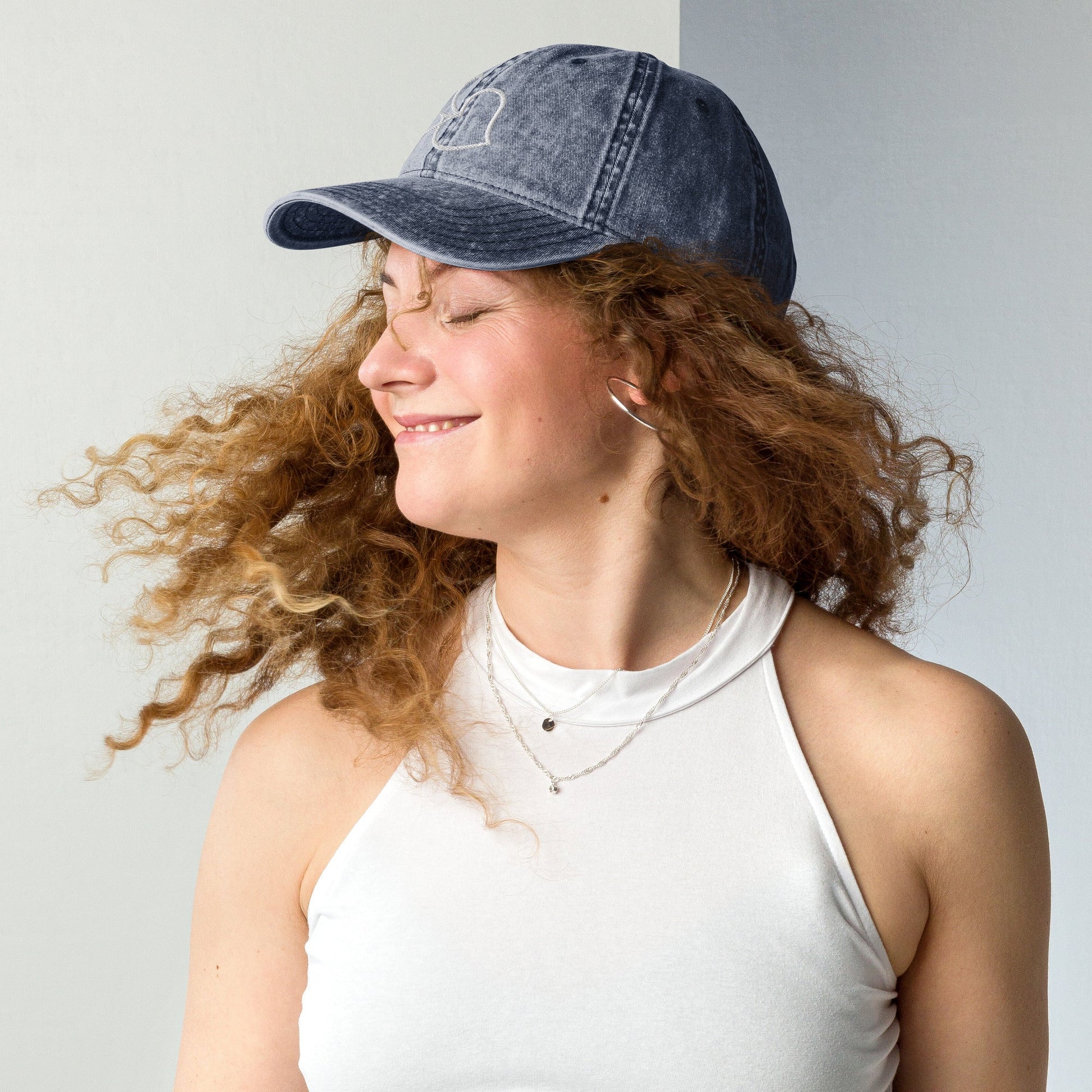 Model twirling in Bare Life’s navy Cocoa-Chic Cap, smiling with curly hair flowing and wearing a white tank top.