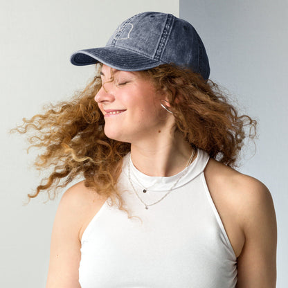 Model twirling in Bare Life’s navy Cocoa-Chic Cap, smiling with curly hair flowing and wearing a white tank top.