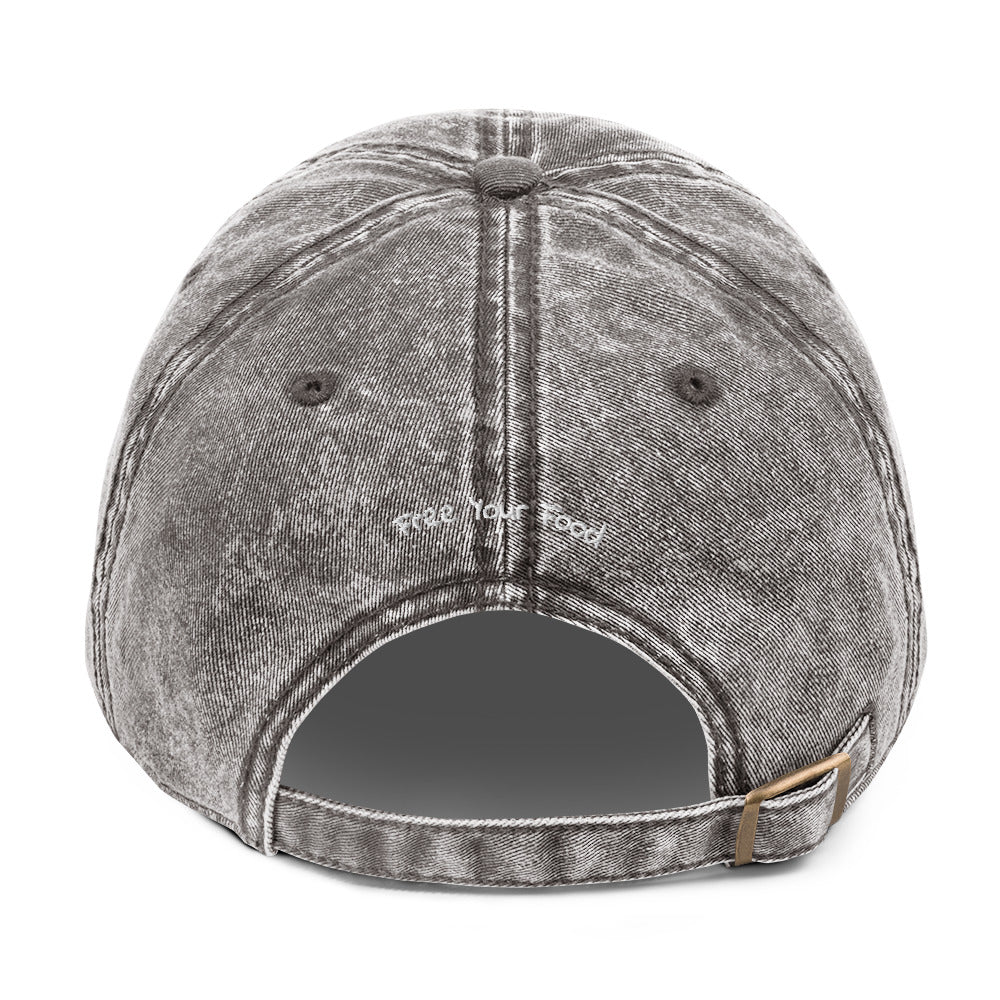 Back view of Bare Life's charcoal gray denim Cocoa-Chic Cap with 'Free Your Food' embroidered above the opening and antique brass buckle strap.