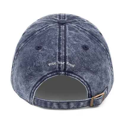 Back view of Bare Life's navy denim Cocoa-Chic Cap with 'Free Your Food' stitched above the adjustable antique brass buckle strap.